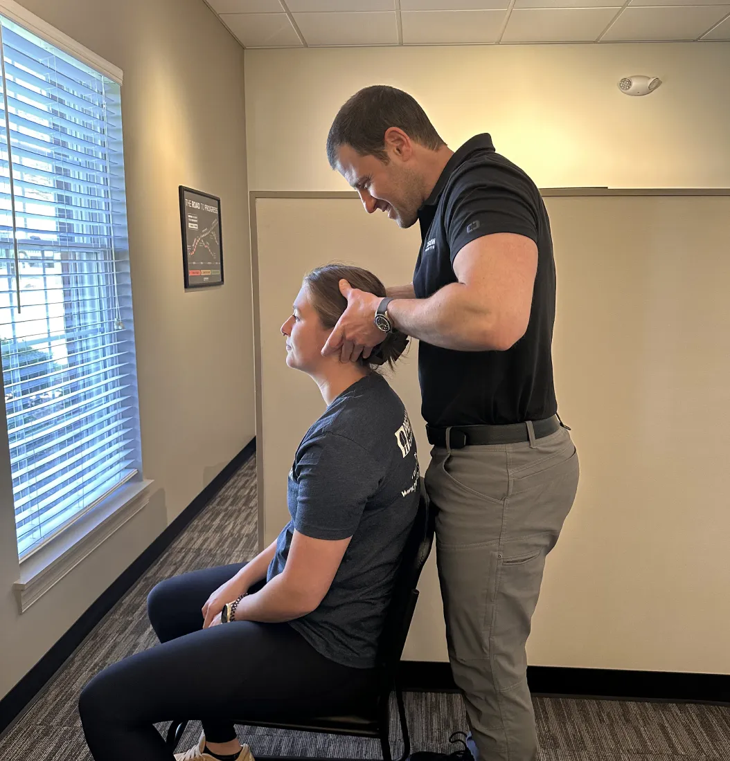 Corrective care chiropractor Matt Westheimer stands behind a sitting female patient and performs a neck adjustment