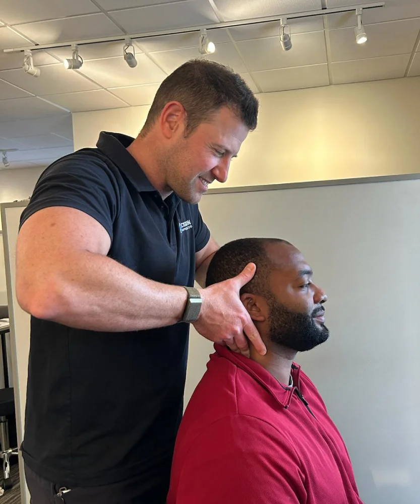 Matthews chiropractor stands behind a seated male patient and performs a chiropractic adjustment as neck pain treatment